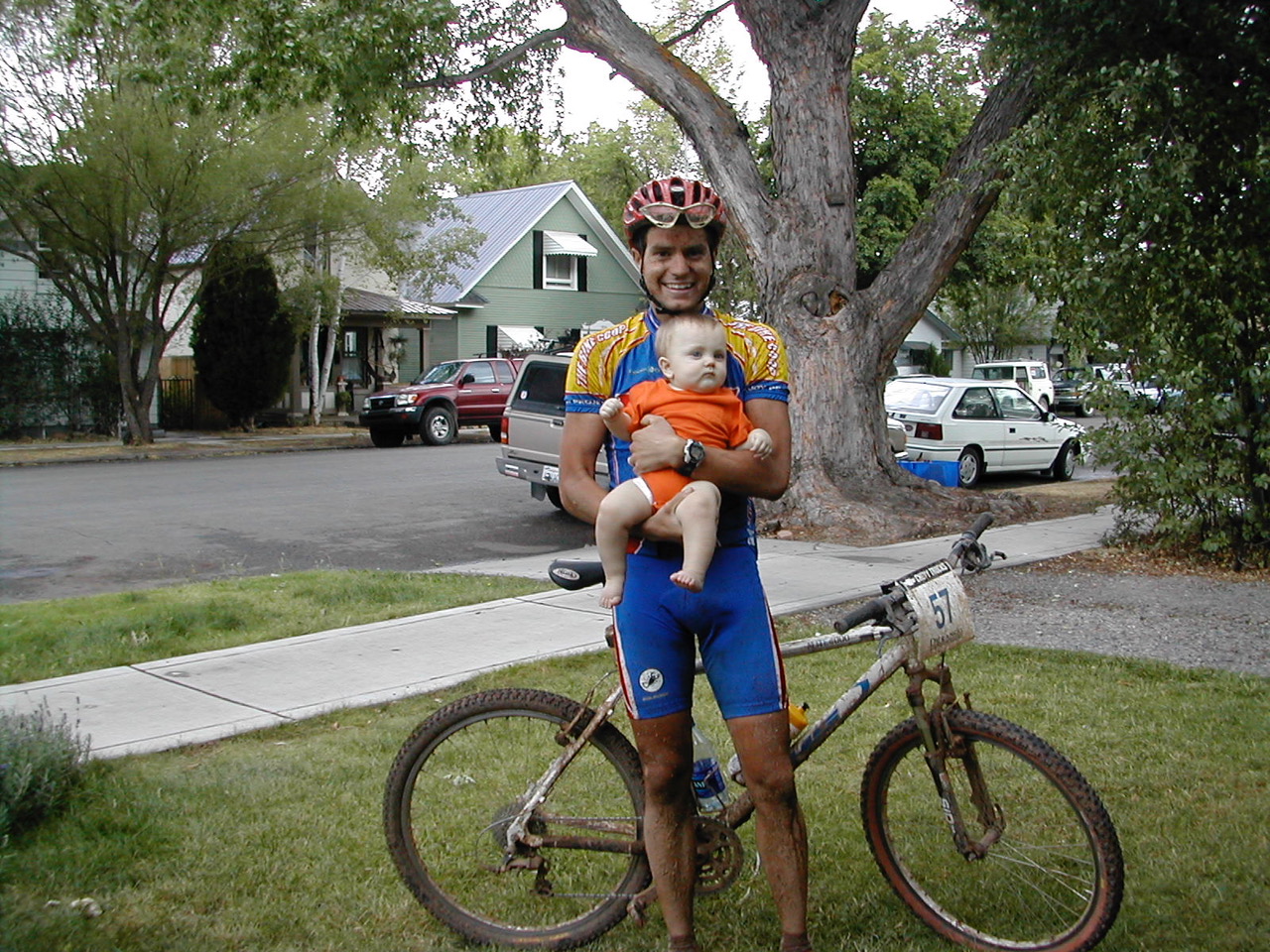 Photo: Doug Campbell, standing with mountain bike and wearing dirty mountain biking outerwear, holding his baby son